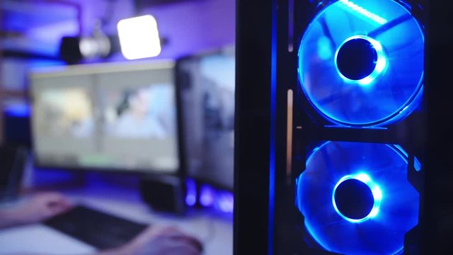 RGB lights PC fans of a professional gamer 4K. Close up shot of PC fans spinning in focus with a computer screens in background of person playing game and streaming himself.