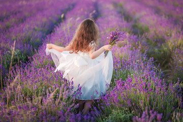 Beautiful young girl in a white dress walking with a bouquet in a lavender field