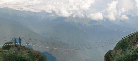 Empty suspension bridge high in the mountains on the background of clouds.