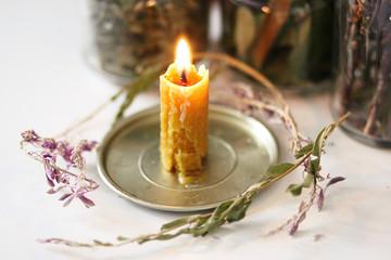 Candle of wax, made by hand, with magic herbs, behind which are jars with the same herbs