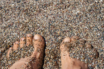 Feet in the sand. Feet covered with small pebbles on the sea beach