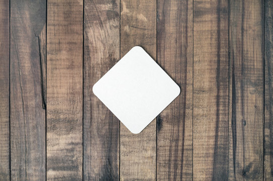 Blank square beer coaster on wood table background. Responsive design mockup. Flat lay.