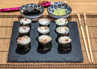Sushi is a dish made from steamed white rice, rolled in gim with salmon and other ingredients with caviar and served in bite-size slices. Wasabi sauce in saucer.