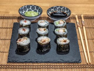 Sushi is a dish made from steamed white rice, rolled in gim with salmon and other ingredients with caviar and served in bite-size slices. Wasabi sauce in saucer.