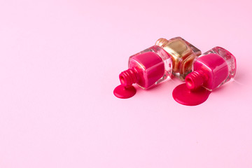 Cosmetic pink and gold nail polishes on a pink background