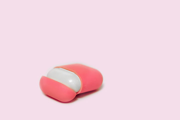 Little white earphones with charger box in bright pink cover box, chosen focus. White background, copy space, close up.
