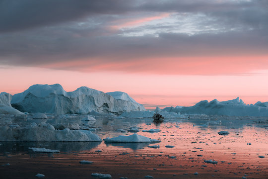 Small boat in front of a floating Iceberg in Greenland during sunset