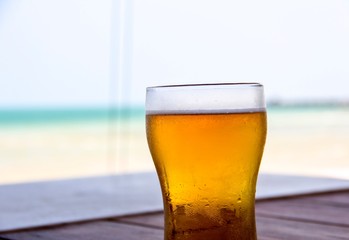 Closeup a fresh cold glass of beer on wooden table beside the beach with blurred background 