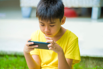 isolated lifestyle portrait of 7 or 8 years old Asian child focused and concentrated playing with mobile phone outdoors at home garden in kid suffering gaming addiction