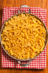 various uncooked raw pasta in a classical metal bowl with red dishtowel in rustic style