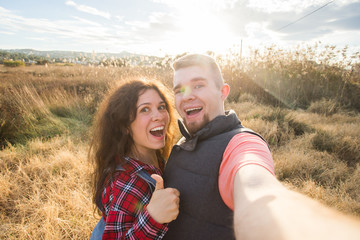 Travel, vacation and holiday concept - Happy couple having fun taking selfie against background on the field and sunset