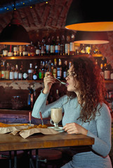 The girl drinks coffee at the bar. The concept of love, the first date, valentine day. Many alcoholic beverages on the shelves.