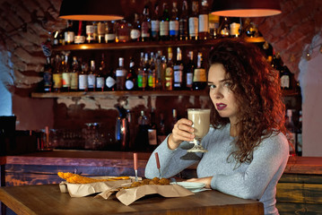 The girl drinks coffee at the bar. The concept of love, the first date, valentine day. Many alcoholic beverages on the shelves.