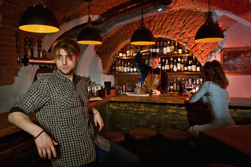 The boy and girl rest in the bar. Couple drinking alcohol. The barman in the background. The concept of love, the first date, valentine day. Many alcoholic beverages on the shelves.