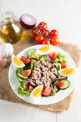 Fresh fish tuna salad made of tomato, ruccola, tuna, eggs, arugula, crackers and spices. Caesar salad in a white bowl on wooden background
