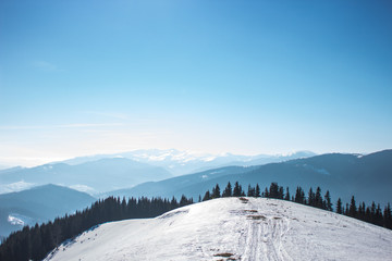 Fototapeta na wymiar Snow-capped mountains and hills. Mountains Carpathians in Ukraine. Winter mountain landscape. Mountain Bukovel. Panorama from the top of the mountain. Freeride ski slope. Skiing and snowboarding.