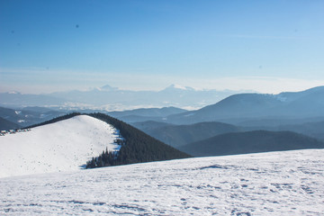 Fototapeta na wymiar Snow-capped mountains and hills. Mountains Carpathians in Ukraine. Winter mountain landscape. Mountain Bukovel. Panorama from the top of the mountain. Freeride ski slope. Skiing and snowboarding.