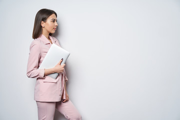 Confident business woman wearing pink suit with laptop underarm