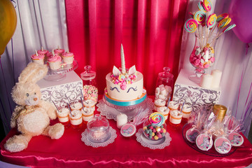 Sweet table and big unicorn cake for baby girl first birthday. Candy bar with a lot of different candies and sweet cakes