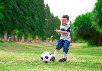 lifestyle portrait at grass city park of 5 years old Asian Indonesian kid playing football happy and excited kicking the ball smiling cheerful in child sport practice education