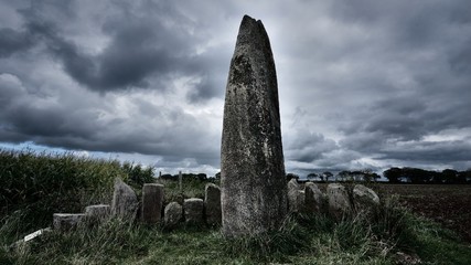 View of Menhir de Prat Ledan with dramatic gray clouds in Brittany, France