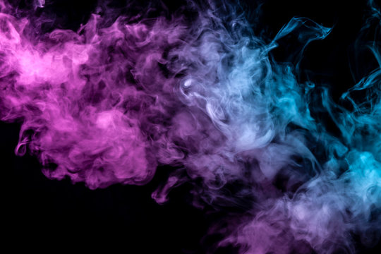 Translucent, thick smoke, illuminated by light against a dark background, divided into three colors: blue, green and purple, burns out, evaporating from a steam of vape.