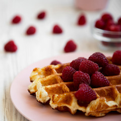 Traditional belgian waffle with raspberries on pink plate on a white wooden table, side view. Closeup.