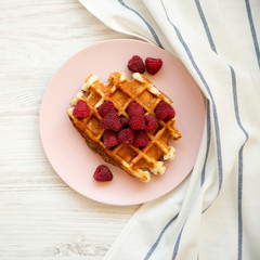 Top view, traditional belgian waffle with raspberries on pink plate over white wooden surface. Overhead, from above.
