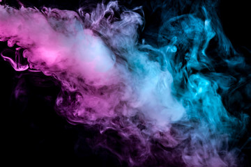 Translucent, thick smoke, illuminated by light against a dark background, divided into three colors: blue, green and purple, burns out, evaporating from a steam of vape.
