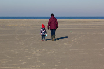 A mother and daughter walking on the beach in the sun in the winter or fall