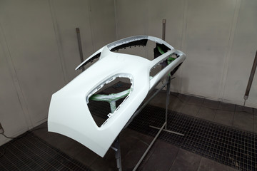 Repair of the rear bumper of a white car after an accident with the help of multi-colored putty in a workshop for painting vehicles in a special chamber