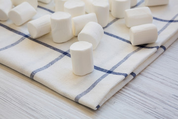Sweet white marshmallows on cloth over white wooden background. Side view.