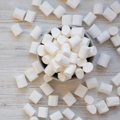 Sweet marshmallows in a bowl over white wooden surface, top view. Flat lay, from above, overhead.