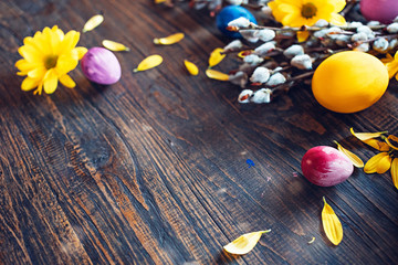 Obraz na płótnie Canvas Easter eggs with blooming twigs of willow and yellow daisy chrysanthemum flowers on a rural wooden table. Hello spring and Easter concept.