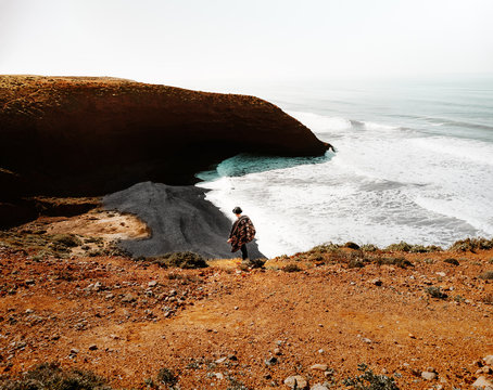 Mann mit einem Poncho und Hut am Legzira Beach bei Sidi Ifni in Marokko