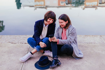 two women friends sitting down at stairs outdoors using laptop computer and having fun.