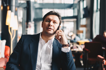 Handsome young businessman in his thirties sitting in a cafe bar during a break from work, talking finance by using a mobile phone. Concept of working on a break.