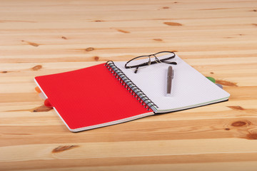 Otwarty czerwony notatnik z piórem, okularami na drewnianym biurku © wojtekm