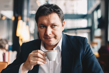 Young and good looking lawyer sitting in a modern restaurant, holding and drinking coffee from a mug.