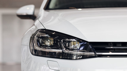 Closeup headlights of a modern white color car. Detail on the front light of a car. Modern and expensive car concept. The car is in the showroom