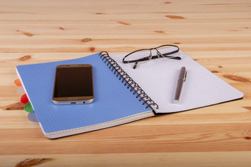 Otwarty niebieski notatnik z piórem, okularami i telefonemna drewnianym biurku © wojtekm