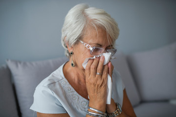 Senior Woman Blowing Nose With Tissue At Home