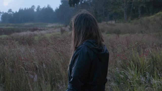 Slow Motion: Young Woman Walking Past Wild Grasses with Trees in the Background