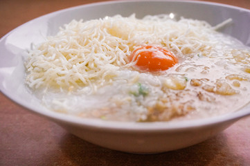 rice porridge in thai style or congee with egg, pork in a white bowl on wood table 