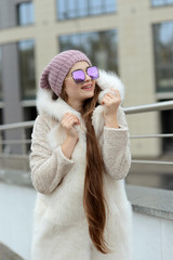 girl in down jacket with fur posing in the city on the background of glass houses