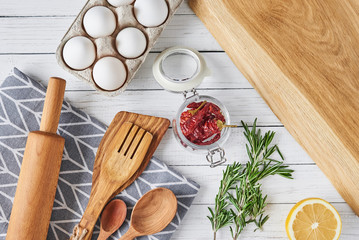 Kitchen utensils and cooking ingredients on a white wooden background, top view