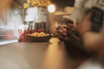 man eating cheesy jalapeno skillet potatoes fries with cheddar and jalapenos from the food truck table at the street food festival in summer night light