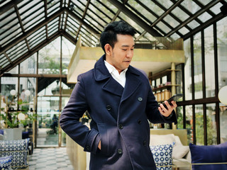 Happy businessman in blue coat using smart phone in cafe.