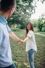 The beautiful brunette girl holds the hand of her beloved husband. Young lovers have fun in nature in the park