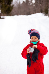 Fototapeta na wymiar Little girl in red winter overall stanind with thermos cup of tea and small biscuit in hand